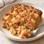Apple cinnamon baked oatmeal on a cream plate with a spoonful beside its tender cut edge.