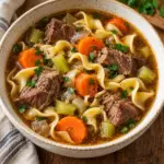 Close view of beef noodle soup with tender chuck, carrots, celery and parsley.