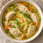 Square overhead bowl of pork dumplings, napa cabbage and carrot in amber broth.