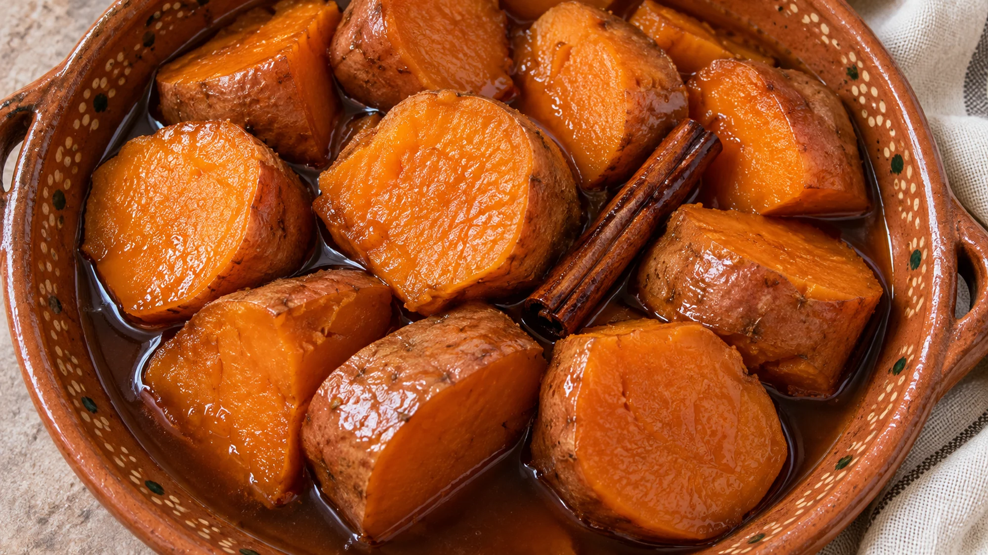 Overhead view of camotes en dulce with a cinnamon stick and dark amber syrup.