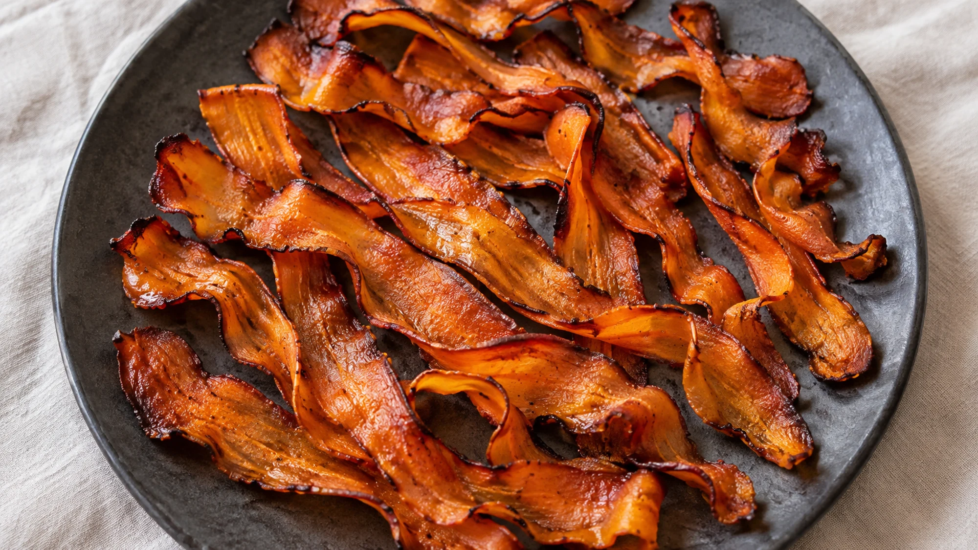 Overhead carrot bacon ribbons with delicate browned edges on a dark plate.