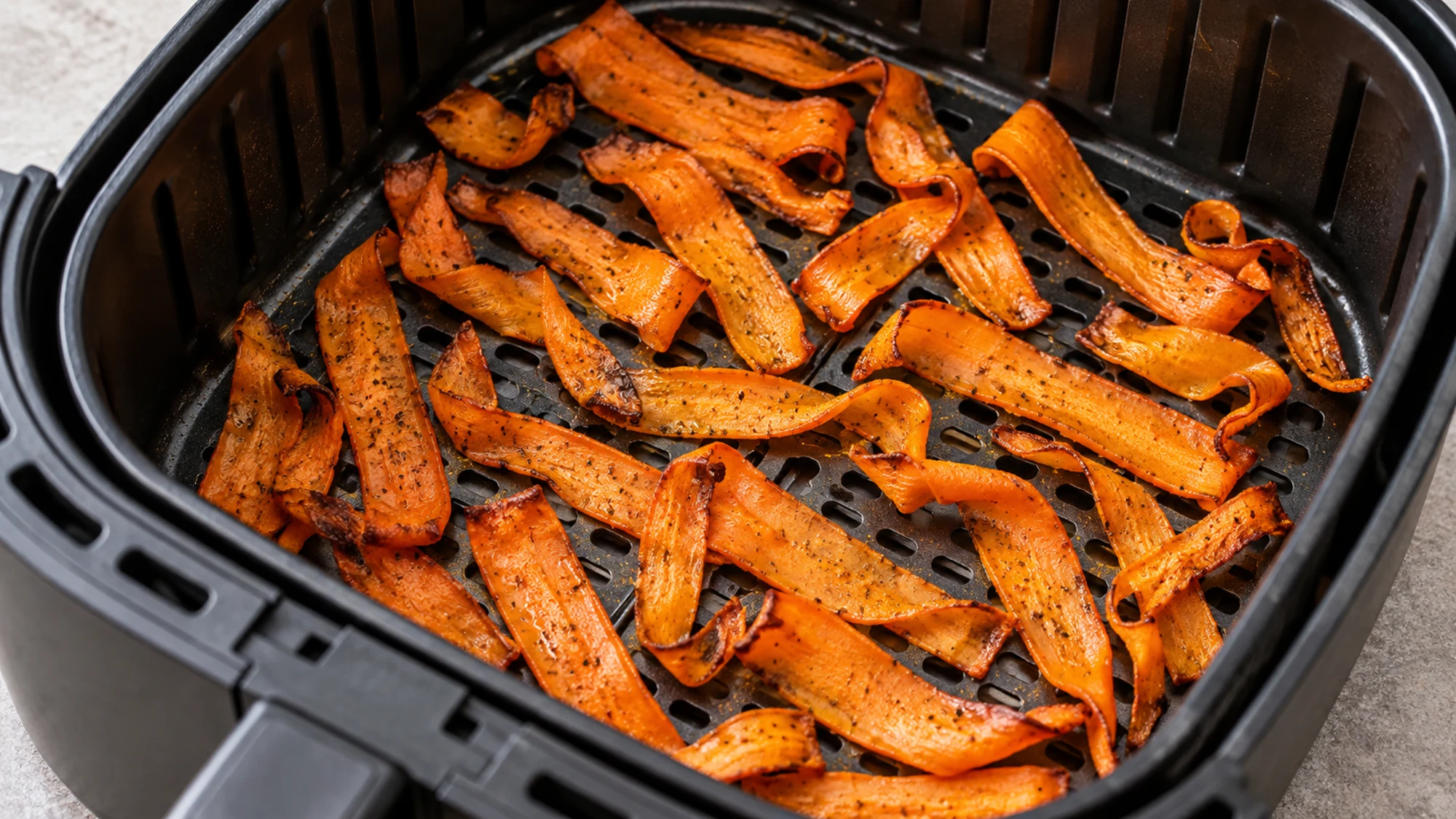 Thin seasoned carrot ribbons in an open air fryer basket.
