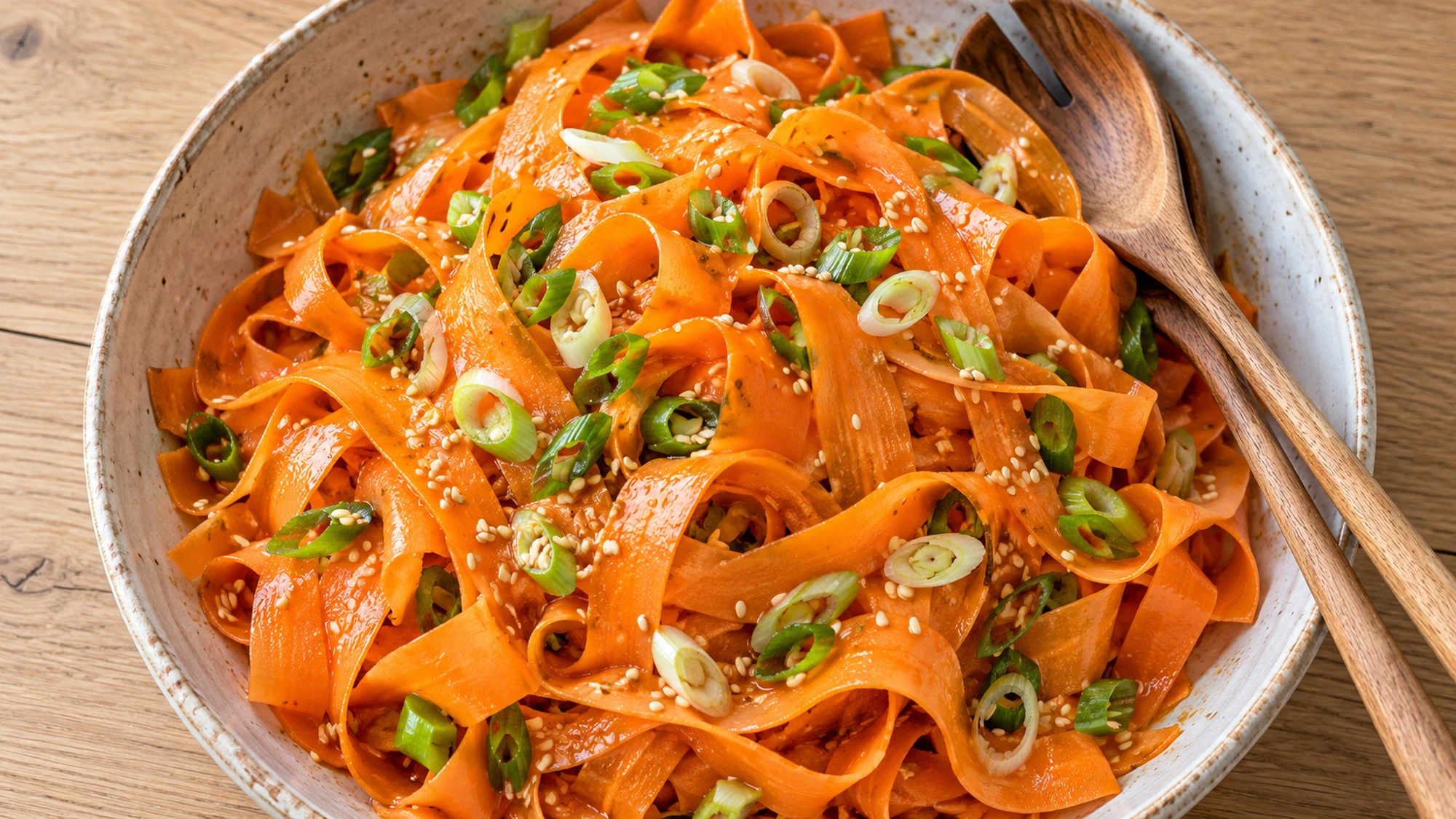Overhead view of dressed carrot ribbons and scallions with wooden salad servers.