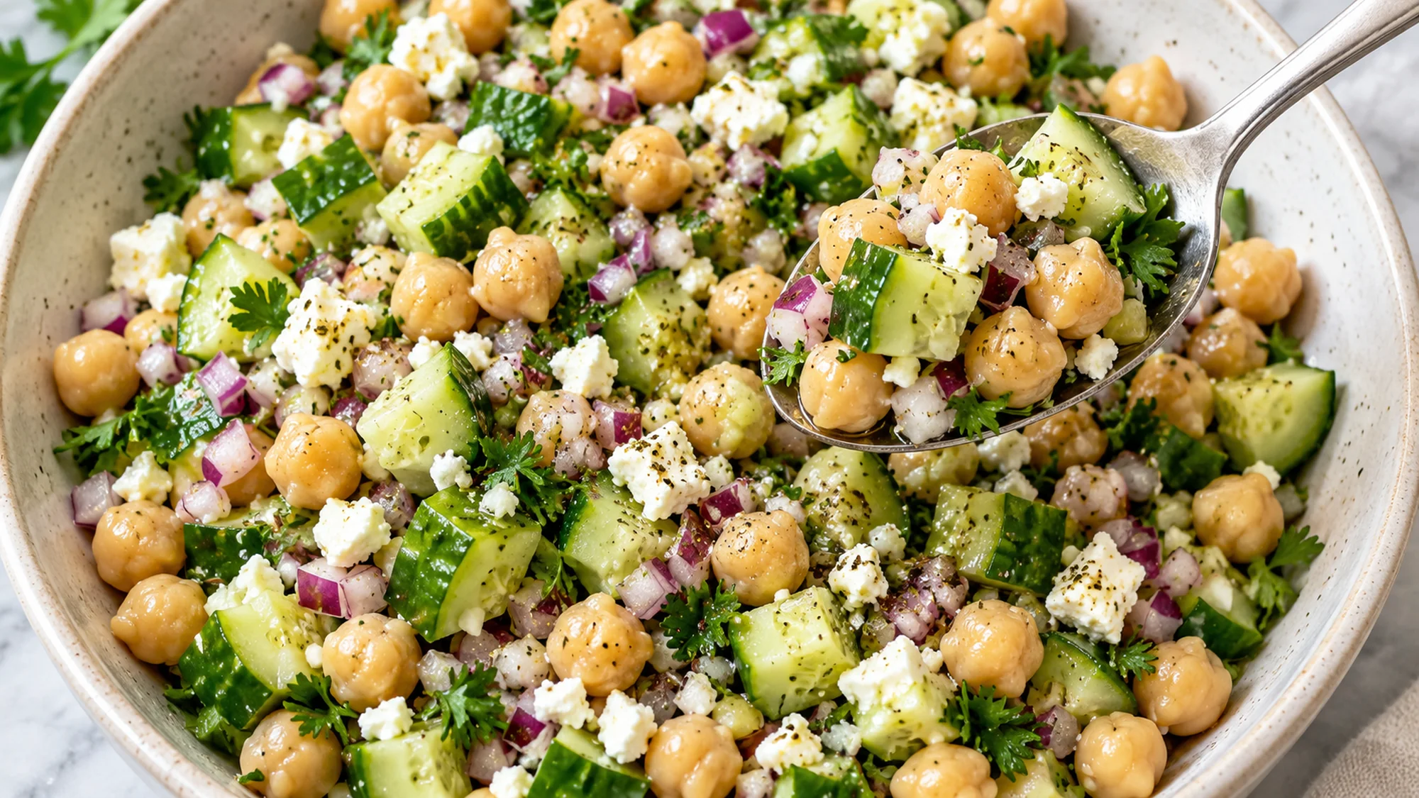 Overhead chickpea cucumber salad with a spoon lifting cucumber, chickpeas and feta