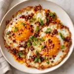 Overhead square view of two chili oil eggs topped with scallions and sesame seeds.