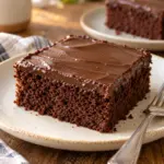 A square of chocolate cake with a thin smooth ganache layer on an ivory plate