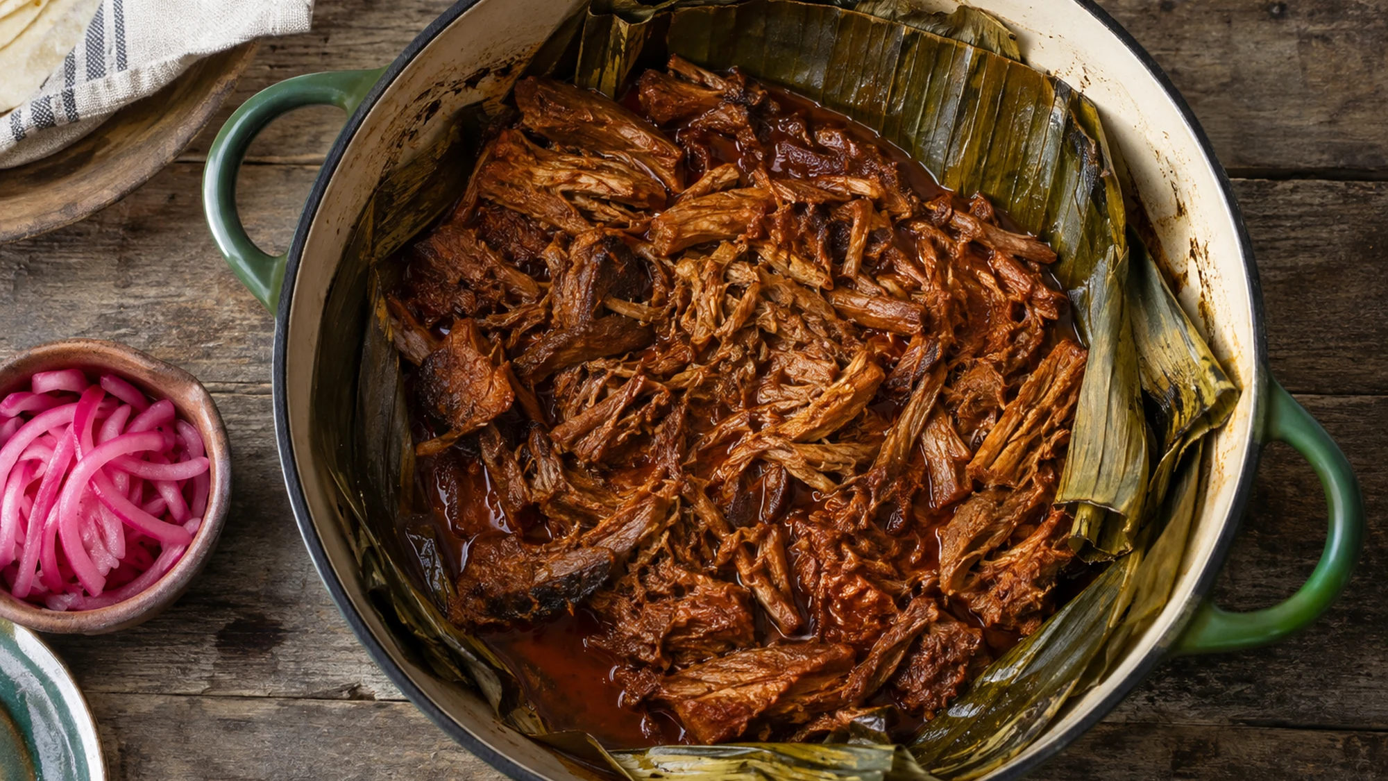 Overhead view of shredded achiote pork in a banana leaf-lined Dutch oven