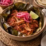Square view of cochinita pibil pork with pickled onion and lime in a banana leaf-lined bowl