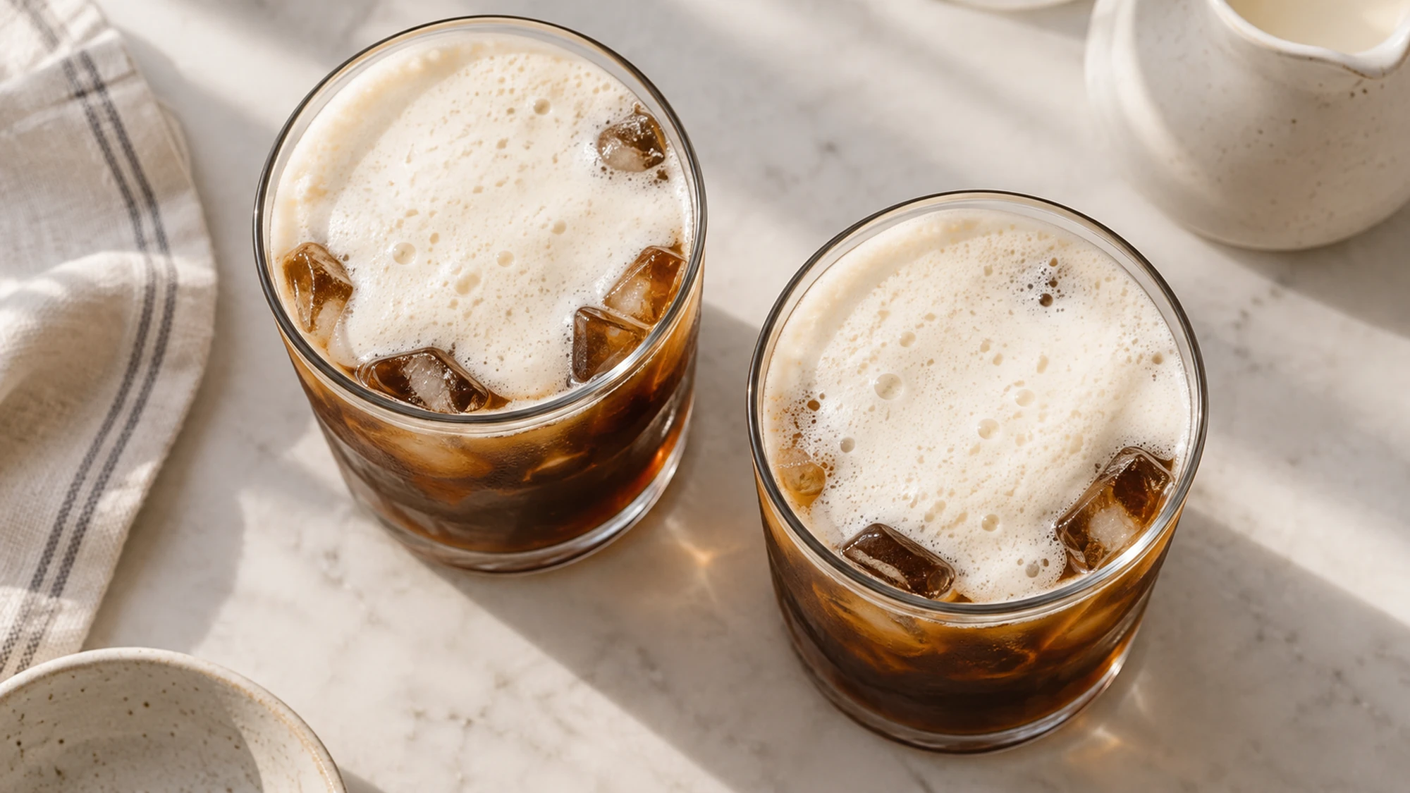 Overhead view of two iced coffees topped with fine-bubbled cold milk foam.