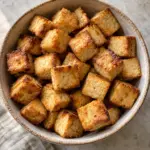 A square composition of golden baked tofu cubes in a bowl.