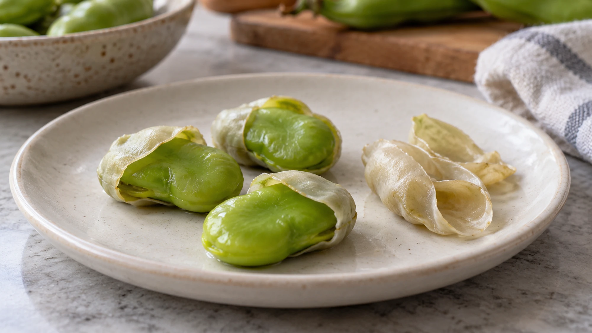 Cooked fava beans with pale seed coats opened to reveal green interiors.