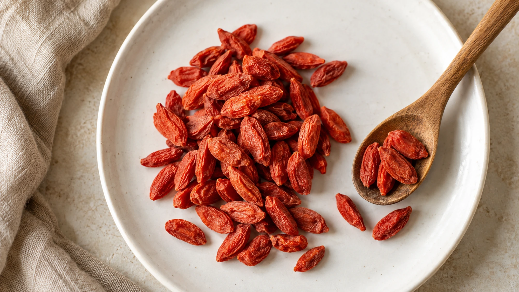 Dried goji berries on a white plate beside a wooden spoon