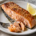 Square close-up of a grilled salmon fillet with flaky flesh and skin underneath.