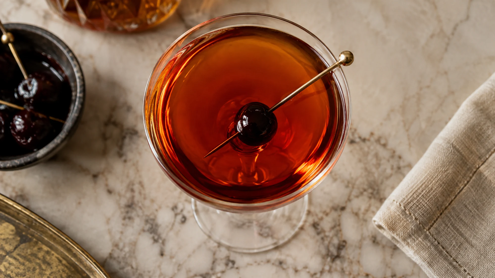 Overhead view of a clear amber Manhattan and cherry garnish.