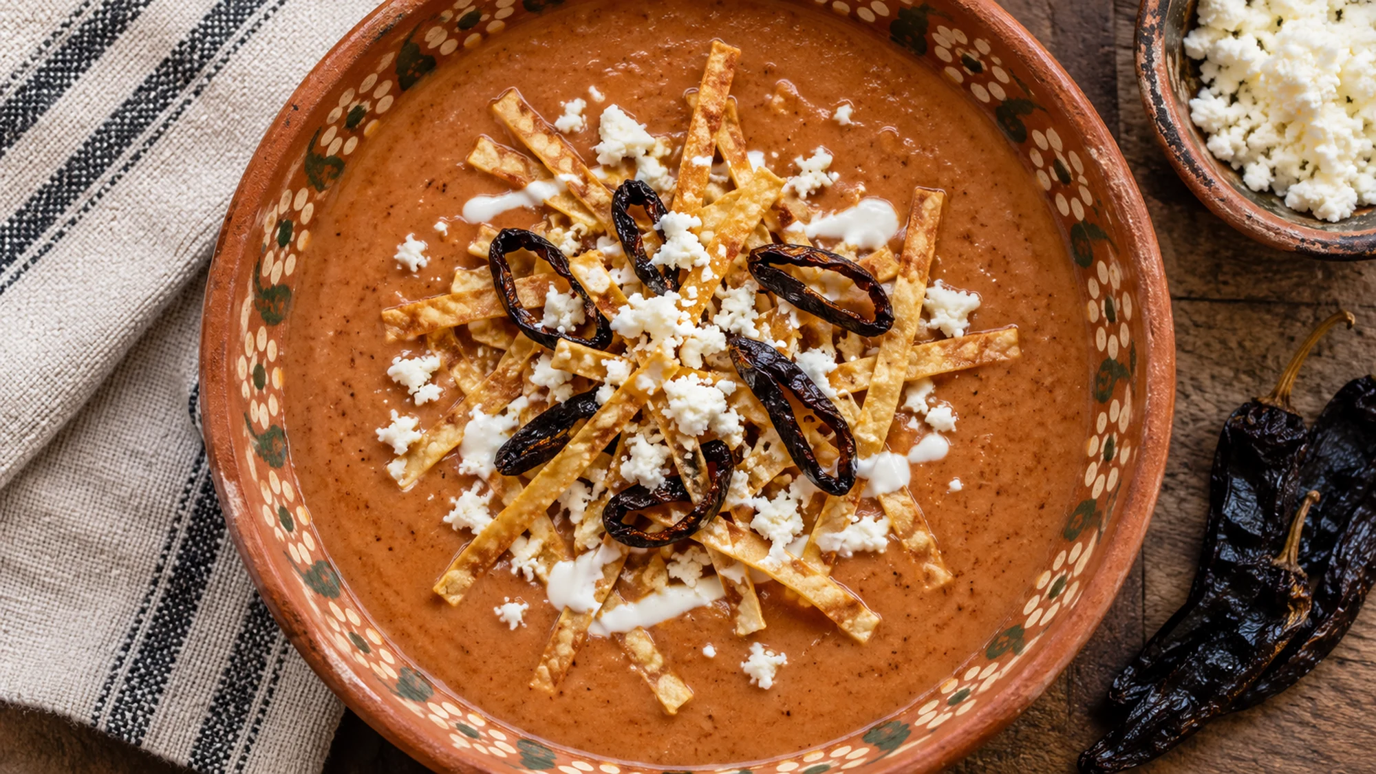 Overhead view of sopa tarasca showing smooth pinto bean soup with crisp tortilla strips and pasilla chile garnish