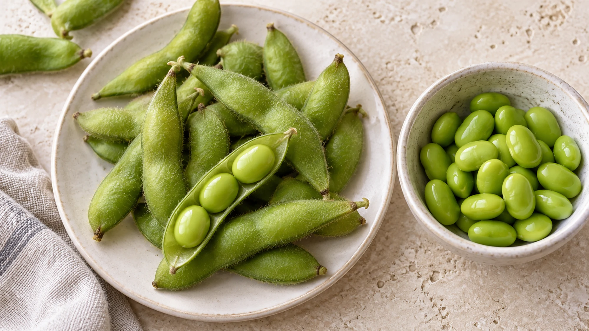 Green edamame pods, an opened pod and shelled beans on a pale surface
