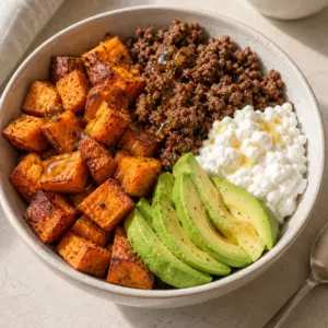 Square view of sweet potato ground beef bowl with roasted potato cubes, cottage cheese, avocado and a little hot honey.