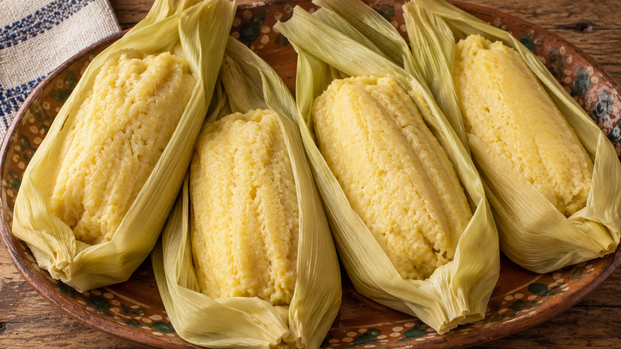 Overhead view of four fresh-corn uchepos on a rustic serving platter.