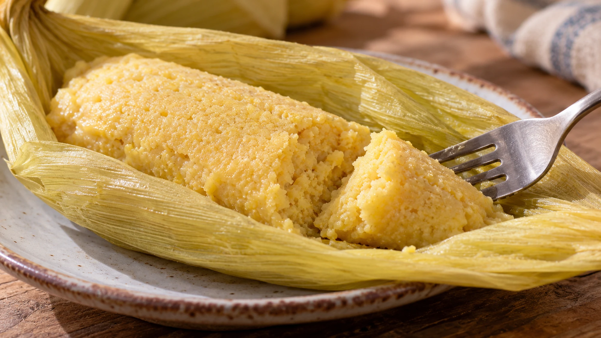 A fork separating a tender bite from an uchepo in its opened corn husk.