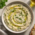 Square overhead bowl of creamy white bean dip with parsley and a measured olive oil swirl.