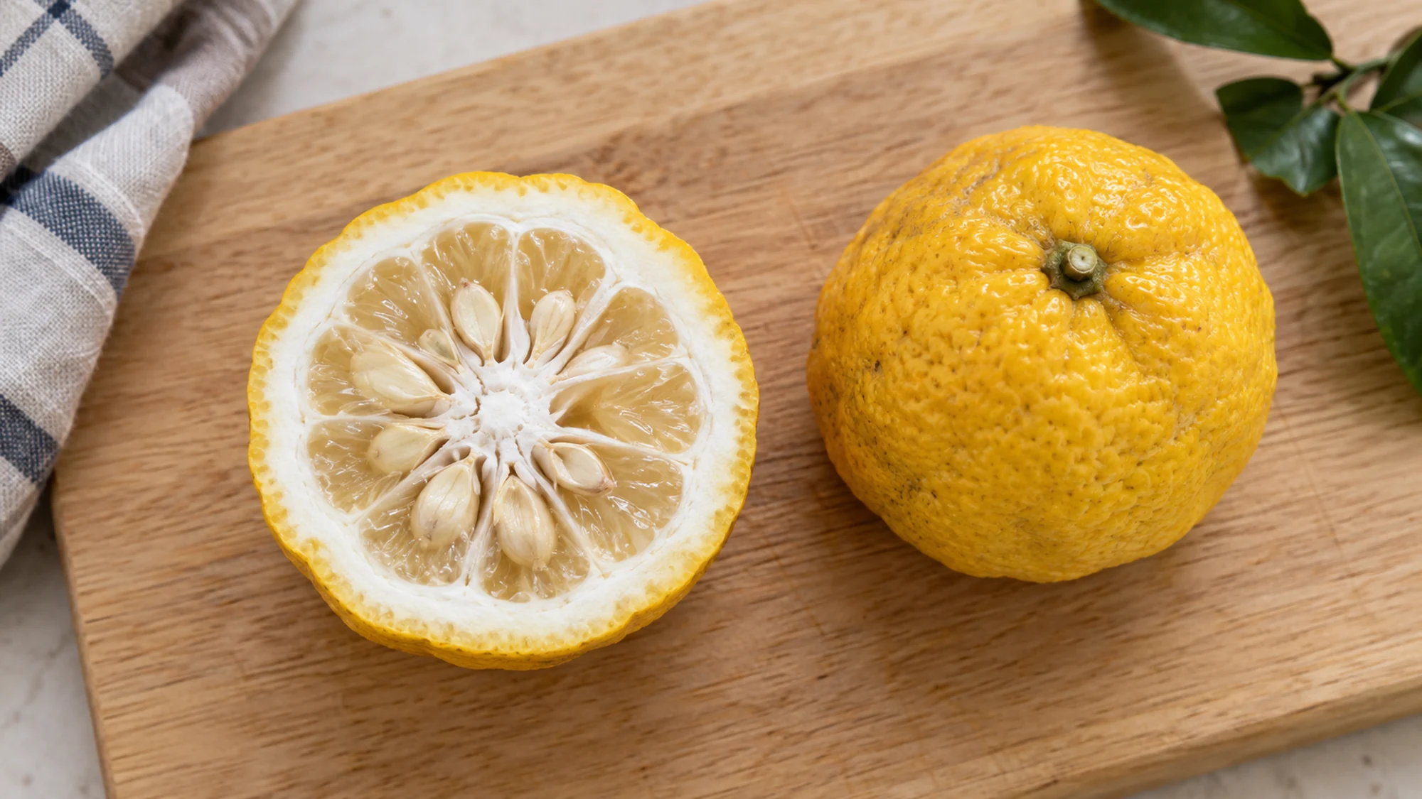 Cut yuzu fruit showing pale flesh, thick white rind and many seeds beside a whole fruit